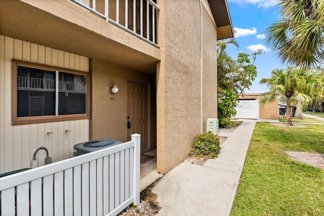 doorway to property with central air condition unit, a yard, and stucco siding