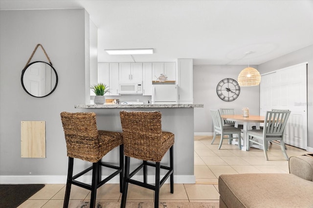 kitchen featuring light tile patterned floors, baseboards, a breakfast bar, white appliances, and white cabinetry