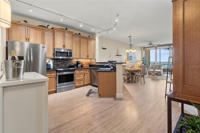 kitchen with light wood-style floors, tasteful backsplash, a ceiling fan, a peninsula, and appliances with stainless steel finishes
