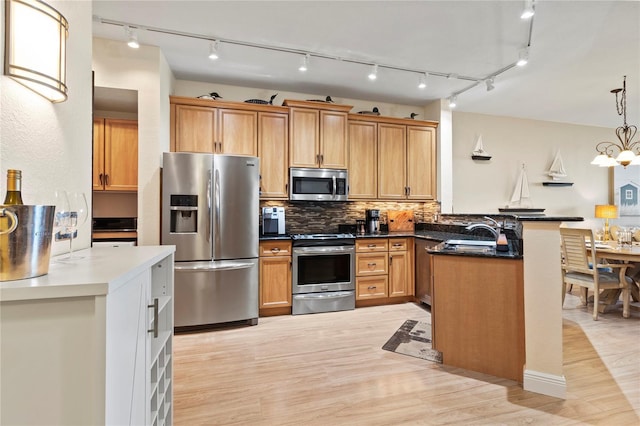 kitchen with decorative backsplash, a sink, stainless steel appliances, light wood finished floors, and a peninsula