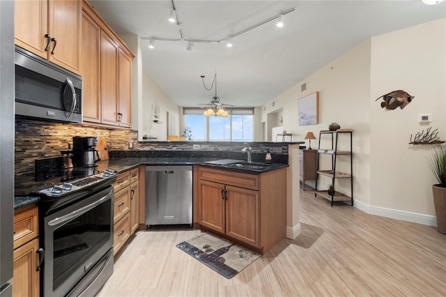kitchen with tasteful backsplash, a sink, appliances with stainless steel finishes, light wood finished floors, and a peninsula