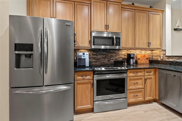 kitchen with dark stone counters, light wood finished floors, brown cabinetry, tasteful backsplash, and appliances with stainless steel finishes