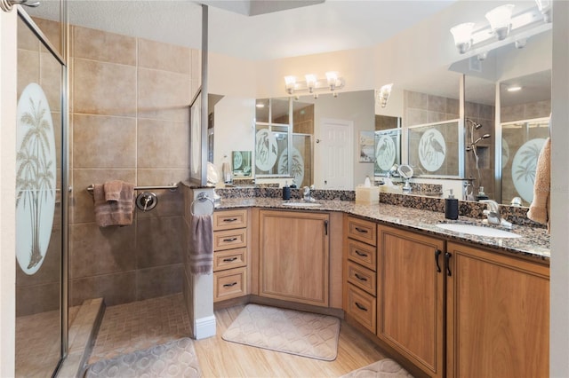 bathroom with a stall shower, wood finished floors, double vanity, and a sink