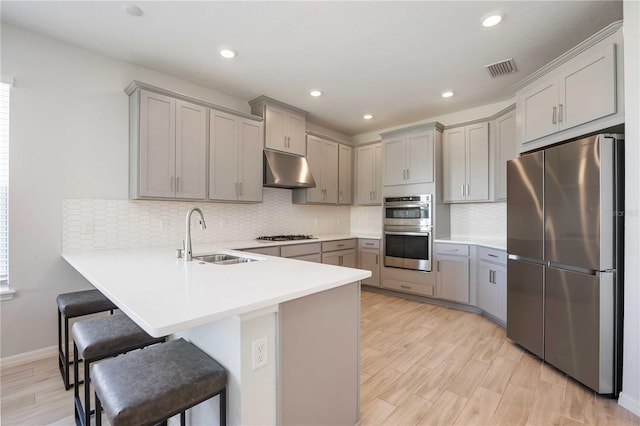 kitchen featuring under cabinet range hood, gray cabinets, appliances with stainless steel finishes, and a sink