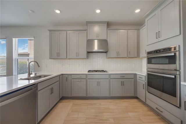 kitchen with under cabinet range hood, light countertops, a sink, gray cabinetry, and appliances with stainless steel finishes