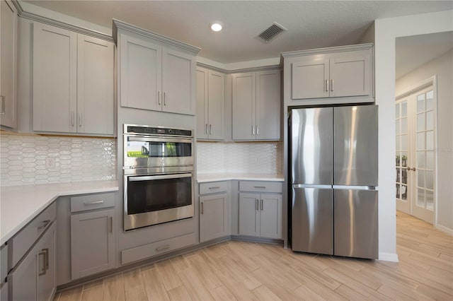 kitchen featuring light countertops, visible vents, gray cabinets, light wood-type flooring, and appliances with stainless steel finishes