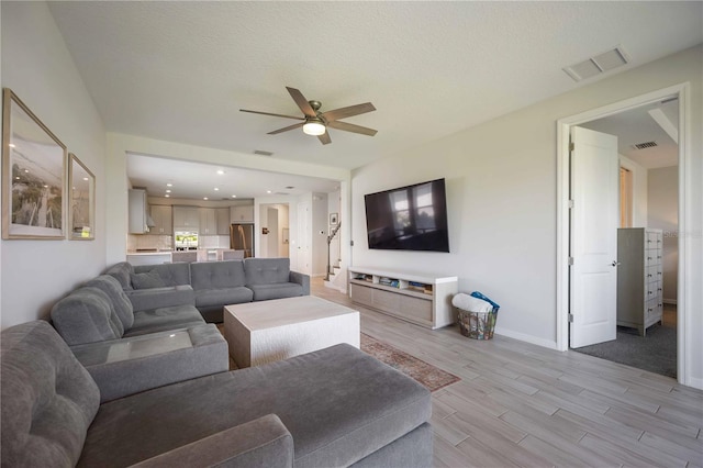 living area with light wood-type flooring, visible vents, baseboards, and ceiling fan