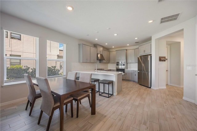 dining area with light wood-type flooring, baseboards, visible vents, and a wealth of natural light