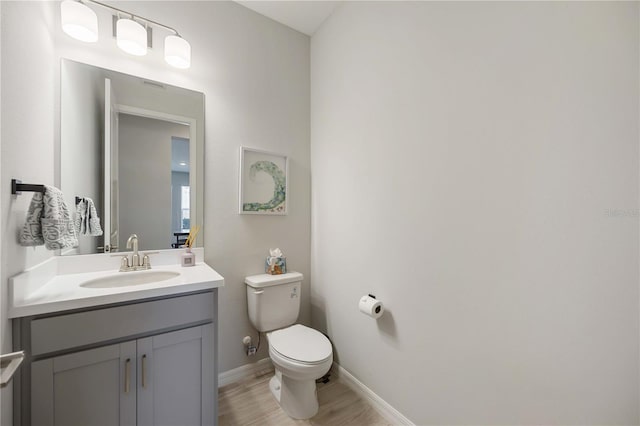 bathroom with baseboards, wood finished floors, vanity, and toilet
