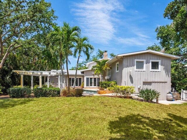 8871 Fishermens Bay Dr, Sarasota, FL 34231 - rear view of house with a lawn, an attached garage, french doors, and a chimney