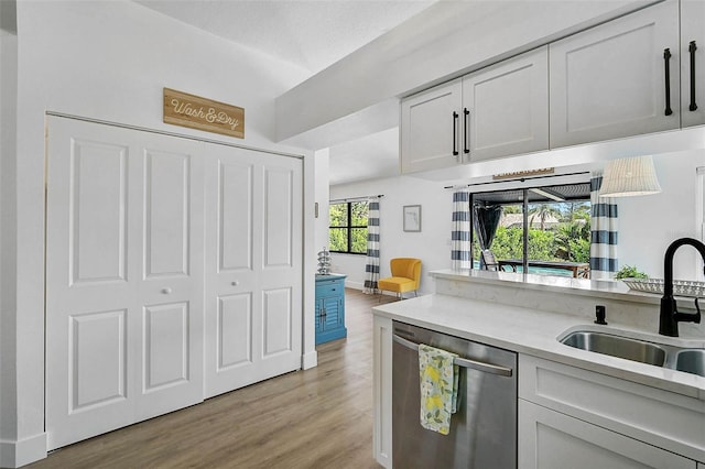 kitchen with dishwasher, a sink, light countertops, light wood finished floors, and white cabinets