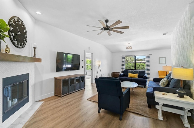living room with ceiling fan, light wood-type flooring, lofted ceiling, a fireplace with flush hearth, and baseboards