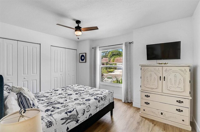 bedroom featuring two closets, light wood-style floors, baseboards, and a ceiling fan