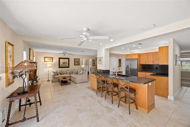 kitchen with a sink, a breakfast bar area, light tile patterned floors, backsplash, and stainless steel refrigerator with ice dispenser