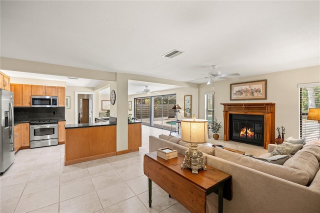 living room featuring a ceiling fan, visible vents, a glass covered fireplace, and light tile patterned floors