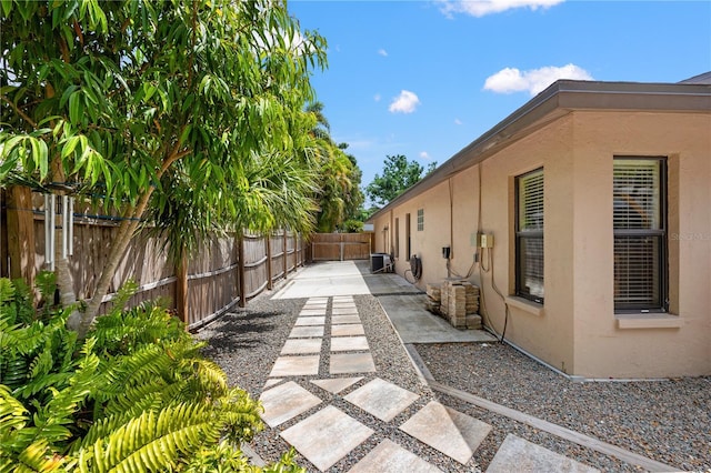 view of side of home with central AC, a fenced backyard, a patio area, and stucco siding