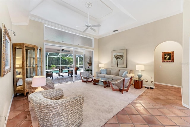 tiled living area featuring a sunroom, a ceiling fan, crown molding, baseboards, and a towering ceiling