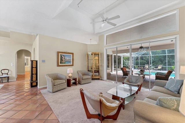 tiled living room featuring a sunroom, a ceiling fan, arched walkways, a towering ceiling, and baseboards