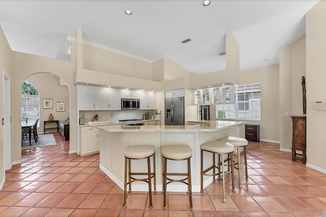 kitchen with appliances with stainless steel finishes, arched walkways, light tile patterned floors, baseboards, and crown molding