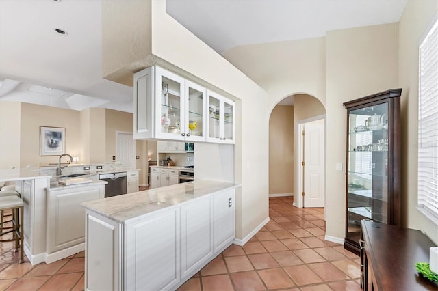 kitchen featuring a peninsula, arched walkways, glass insert cabinets, a sink, and white cabinetry