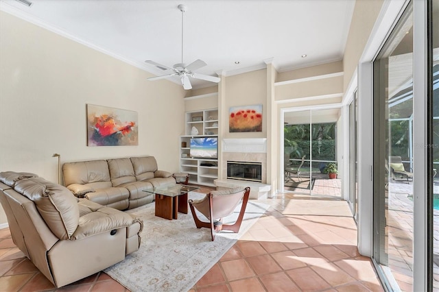 living room with ornamental molding, tile patterned flooring, a ceiling fan, a glass covered fireplace, and built in features