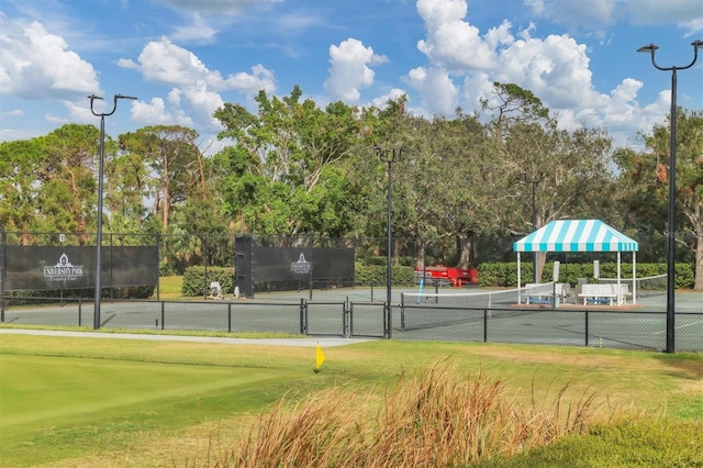 view of tennis court with view of wooded area and a gate