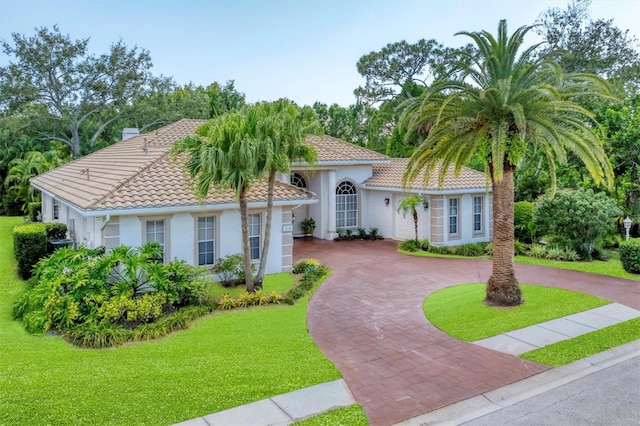 mediterranean / spanish-style house featuring stucco siding, curved driveway, a front yard, and a tiled roof