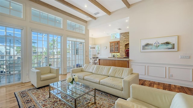 living room with a towering ceiling, beamed ceiling, wood finished floors, and a wealth of natural light
