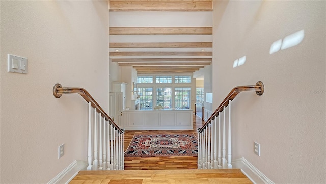 stairway with baseboards, beam ceiling, and wood finished floors