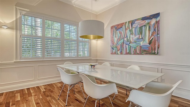 dining space with crown molding, a wainscoted wall, a decorative wall, and wood finished floors