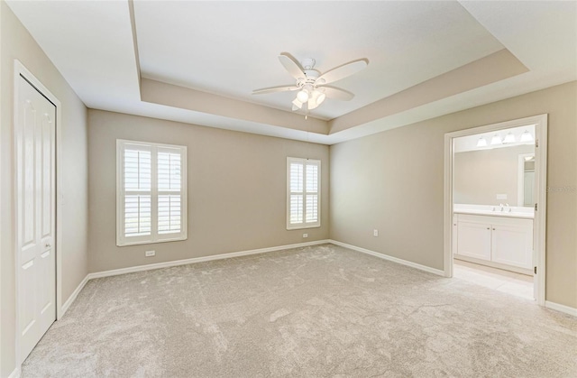 unfurnished bedroom with baseboards, light colored carpet, and a tray ceiling
