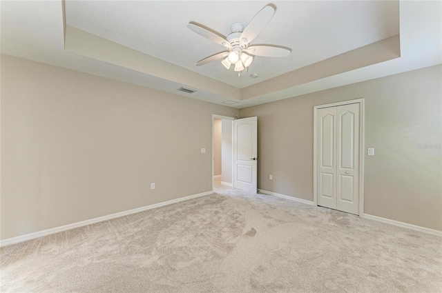 unfurnished bedroom featuring a raised ceiling, visible vents, a closet, baseboards, and carpet floors