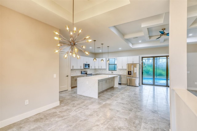 22 Medalist Cir, Rotonda West, FL 33947 - kitchen with decorative backsplash, a raised ceiling, stainless steel appliances, a center island, and ceiling fan with notable chandelier