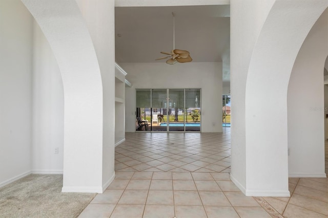 interior space featuring arched walkways, baseboards, a towering ceiling, ceiling fan, and light tile patterned floors