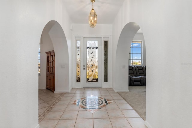 tiled foyer featuring arched walkways, baseboards, and a chandelier