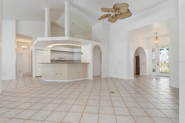 unfurnished living room featuring high vaulted ceiling, arched walkways, ceiling fan with notable chandelier, and light tile patterned floors