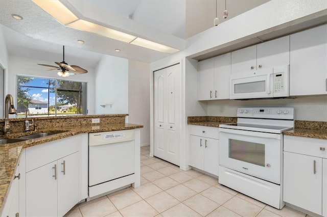kitchen with white cabinets, a sink, dark stone countertops, light tile patterned flooring, and white appliances