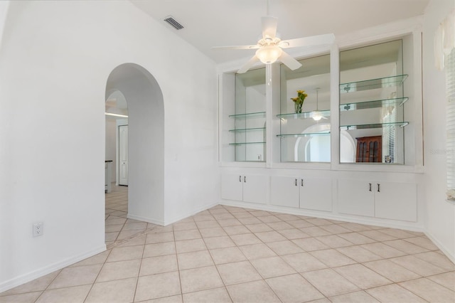 empty room featuring a ceiling fan, arched walkways, baseboards, tile patterned flooring, and visible vents