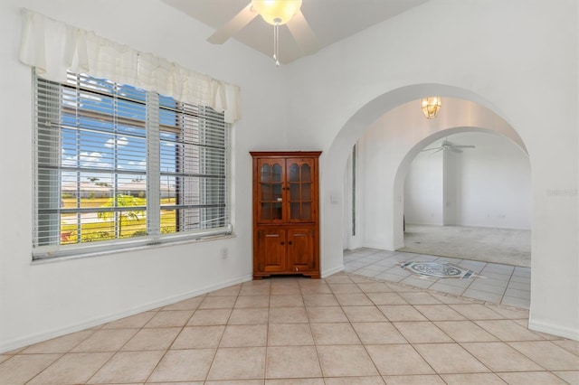 unfurnished room with light colored carpet, ceiling fan, arched walkways, and light tile patterned floors