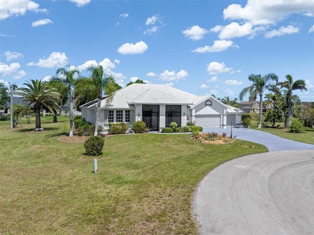 view of front of property featuring a tiled roof, an attached garage, a front lawn, and driveway