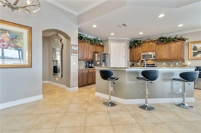 kitchen with a breakfast bar, brown cabinetry, stainless steel appliances, backsplash, and visible vents