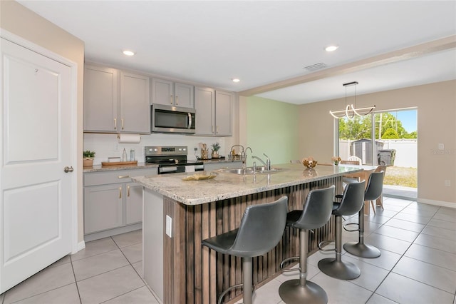 2969 Great Abaco Way, Bradenton, FL 34208 - kitchen featuring stainless steel appliances, gray cabinetry, a sink, light stone counters, and a kitchen breakfast bar