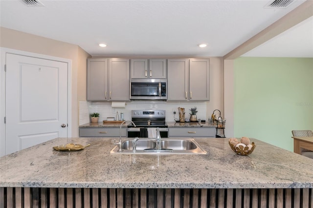 2969 Great Abaco Way, Bradenton, FL 34208 - kitchen featuring stainless steel appliances, a sink, gray cabinets, tasteful backsplash, and light stone counters