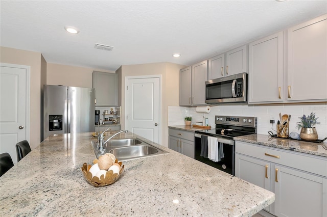 2969 Great Abaco Way, Bradenton, FL 34208 - kitchen with stainless steel appliances, a sink, decorative backsplash, gray cabinetry, and a center island with sink