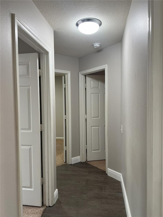 hall featuring baseboards, a textured ceiling, and dark wood finished floors