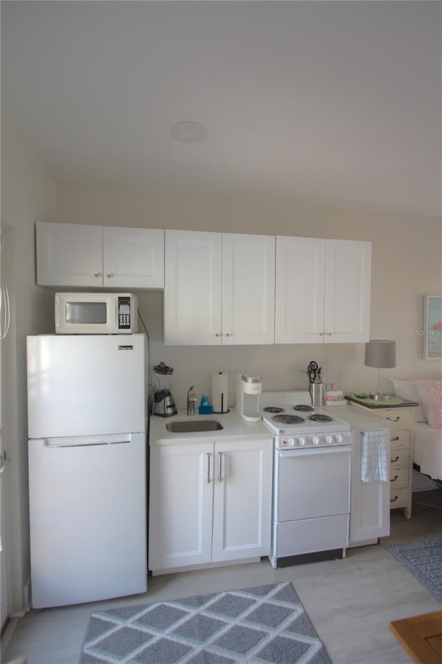 kitchen with white cabinets, light countertops, white appliances, and a sink