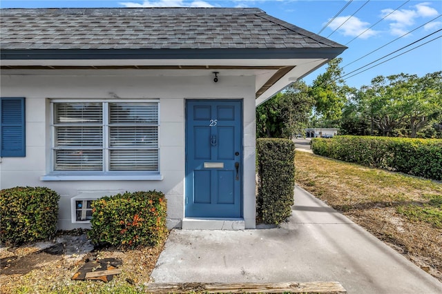 view of exterior entry featuring stucco siding and roof with shingles