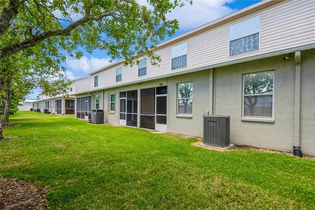 rear view of property featuring central air condition unit, a yard, and stucco siding