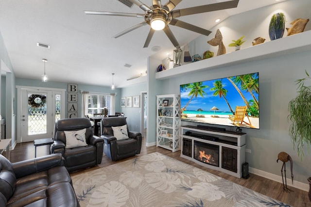 living room with a ceiling fan, visible vents, vaulted ceiling, wood finished floors, and baseboards