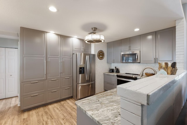kitchen with decorative backsplash, gray cabinets, stainless steel appliances, and light wood-type flooring